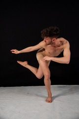 Male body-colored ballet dancer practicing in the studio with hands and legs on a black background. The attractive young man shows modern dance poses.
