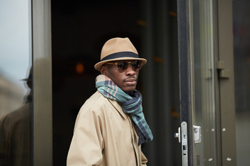 Waist up portrait of modern African-American man wearing hat posing outdoors in city, copy space