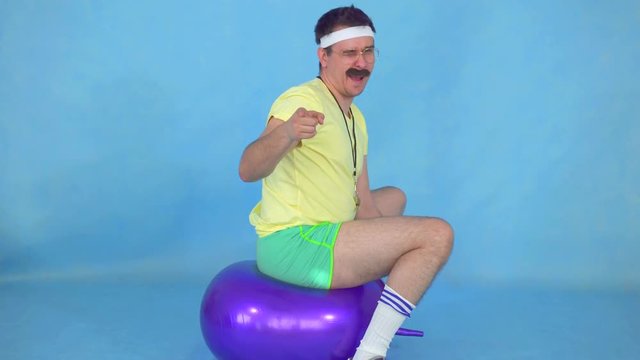 Funny man coach with a mustache from 80's, on the fitness ball on blue background