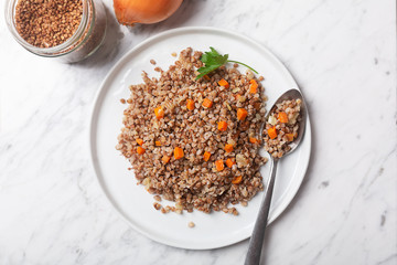 Boiled buckwheat cereal with carrot, parsley and butter in a bowl on a white stone marble background. Traditional Russian dish on gray background with copy space
