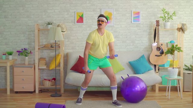 Funny young man with a mustache from the 80's engaged with dumbbells at home