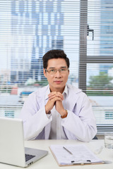 Confident male doctor with stethoscope working in office