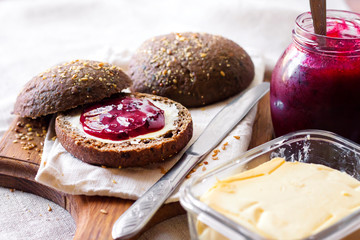 Homemade rye buns with linseeds, sesame and white poppy seeds served with butter and Jostaberry jam
