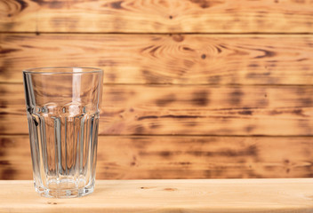 Empty glass on a light wooden table on a wooden background.