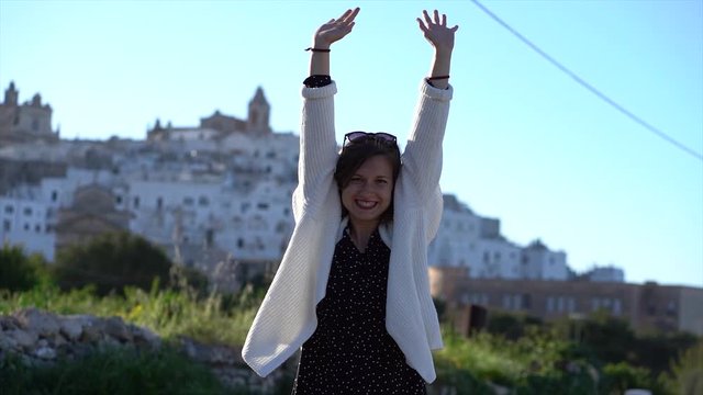 happy tourist shows happiness in front of the white city of ostuni, Apulia region, south italy 