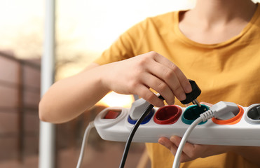 Woman inserting power plug into extension cord indoors, closeup. Electrician's professional...