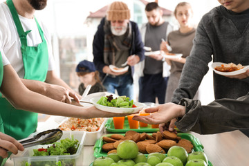 Volunteers giving food to poor people indoors