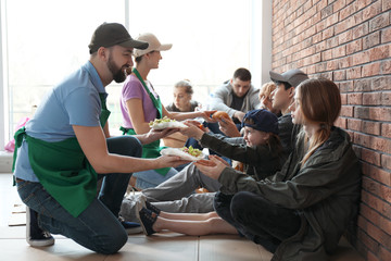 Volunteers giving food to poor people indoors