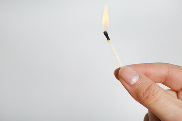 Woman holding burning match on grey background, space for text