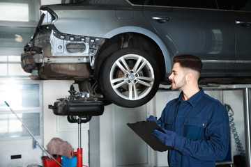 Technician checking car on hydraulic lift at automobile repair shop