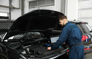 Fototapeta na wymiar Technician checking car with laptop at automobile repair shop