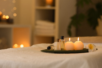 Cosmetics and burning candles on massage table in spa salon, space for text