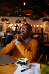 Warm toned portrait of pensive African-American man using laptop sitting at table in cafe