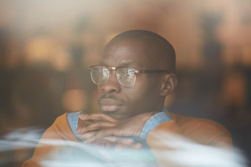 Warm toned portrait of pensive African-American man using laptop sitting by window in cafe