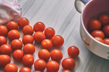 Cherry tomatoes in a purple bowl next to a light coloured checkered napkin on a light wooden background, viewed from above.