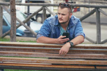 Young man is sitting at the park and using smartphone, phone, calls. concept of remote work, and finding information on the journey