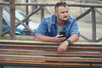 Young man is sitting at the park and using smartphone, phone, calls. concept of remote work, and finding information on the journey