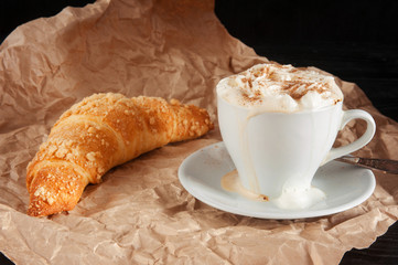 Croissant and cup of coffee with cream. Tasty breakfast.