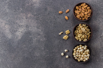 Almonds, walnuts and hazelnuts in wooden bowls on dark concrete background. Top view, copy space