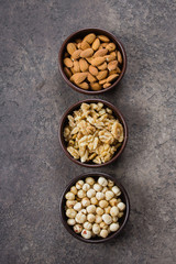 Almonds, walnuts and hazelnuts in wooden bowls on dark concrete background. Top view, copy space