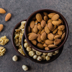 Almonds, walnuts and hazelnuts in wooden bowls on dark concrete background. Top view, copy space