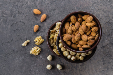 Almonds, walnuts and hazelnuts in wooden bowls on dark concrete background. Top view, copy space