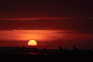 the twilight sky in an airport is decorated with sunsets which start to sink golden orange with silhouettes of aircraft activities around the airport