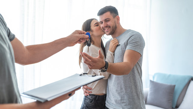 Conceptual man Hand Giving Keys to Happy Young Sweet Couple. Man with his wife being given a house key. Hands of estate agent giving keys to the couple