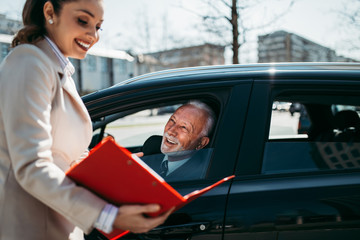 Beautiful young woman sales manager showing car specification to happy senior man buyer.