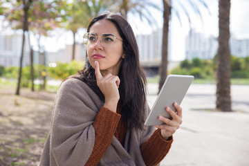 Pensive pretty woman using tablet computer outdoors