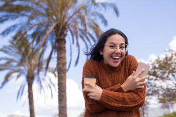 Smiling woman shivering from cold and embracing herself outdoors