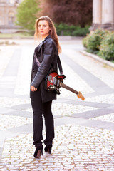 young woman in leather jacket and guitar walking on the street