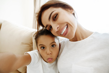 Family. Love. Mom and daughter in pajamas are hugging, looking at camera and smiling while doing selfie at home