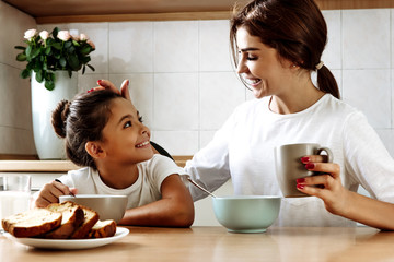 Family. Eating. Home. Mom and daughter are talking and smiling while having lunch in the kitchen at...