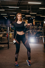 Fototapeta na wymiar Young girl playing dumbbell to exercise in fitness. Photo of sporty caucasian woman in sportswear. Strong abs showing. Noise photo