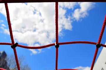 view of the blue sky with clouds through the red rope net