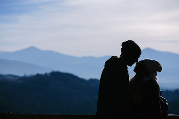 Silhouettes of young couple in love standing on the top of mountain