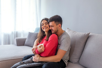 Obraz premium Beautiful couple hugging and looking at each other. Young woman feeling happy and smiling while sitting with her beloved man on the sofa and looking at him while hugging