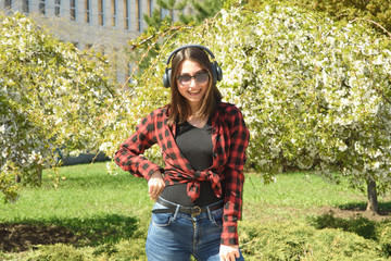 Happy girl listening to music on headphones and dancing in the park