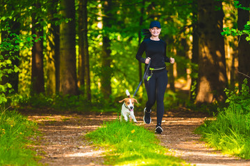 Girl walking with beagle dog outdoors in nature on a path in forest.