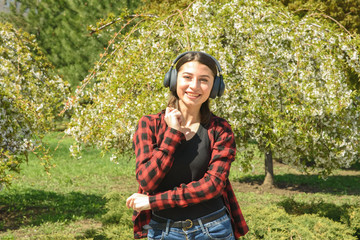 Happy girl listening to music on headphones and dancing in the park