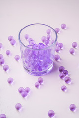 Purple marbles in drinking transparent glass with scattered marbles on white background 