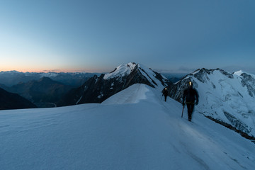 Alpinists on snowy ridge early before sunrise, Aiguille de Bionnassay, Mont Blanc massif, France