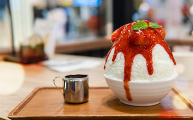 Strawberry Bingsu or Patbongsu serving on the wooden plate and a metal jar of strawberry syrup...
