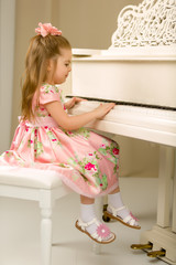 Beautiful little girl is playing on a white grand piano.