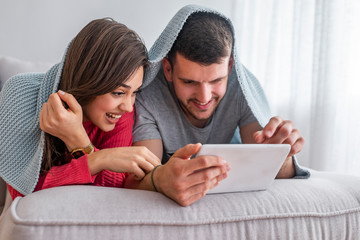 Fototapeta premium Leisure and technology in the bed. Couple having fun with digital tablet in bed. Close up view of beautiful smiling young wife and husband looking a tablet