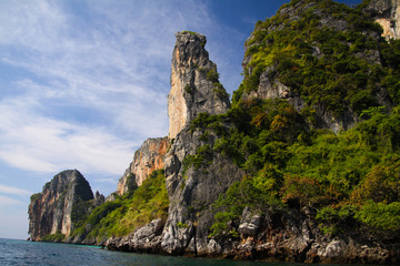 Boat trip along the coast line of tropical island Ko Phi Phi along impressive rock formations under blue sky