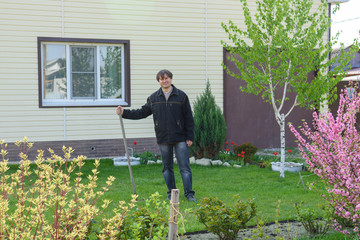 A man rakes old foliage on a green grass lawn at his summer cottage