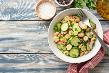 Healthy vegetable salad with cucumber, radish, beans, mini corn and herbs on rustic wooden background. Top view. Copy space.