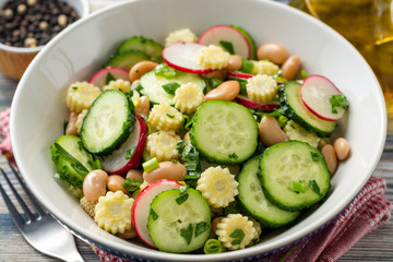 Healthy vegetable salad with cucumber, radish, beans, mini corn and herbs on rustic wooden background. Selective focus.